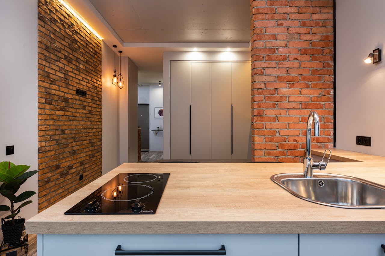 Stylish modern kitchen featuring exposed brick wall, sleek island, and stainless steel fixtures.